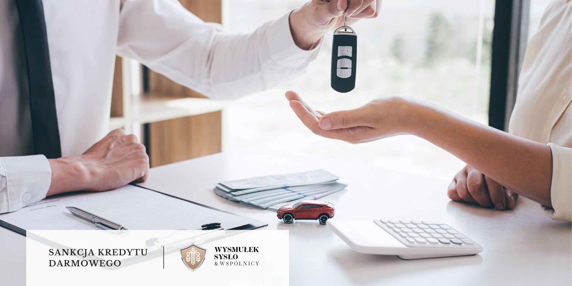 sankcja-kredytu-darmowego-umowa-na-samochod <br />
Człowiek w garniturze przekazuje kluczyki do samochodu. Na stole leży umowa, banknoty, kalkulator oraz miniaturowy, czerwony samochód.