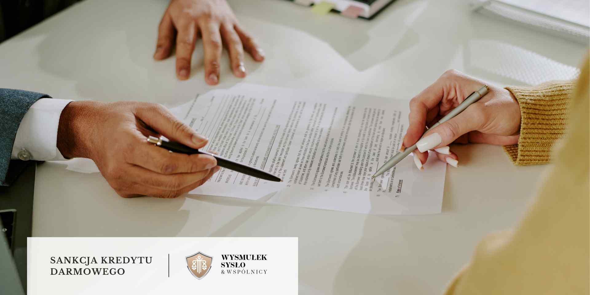 Dwie dłonie, z których jedna trzyma srebrny długopis i podpisuje dokument leżący na białym stole, a druga dłoń spoczywa na dokumencie