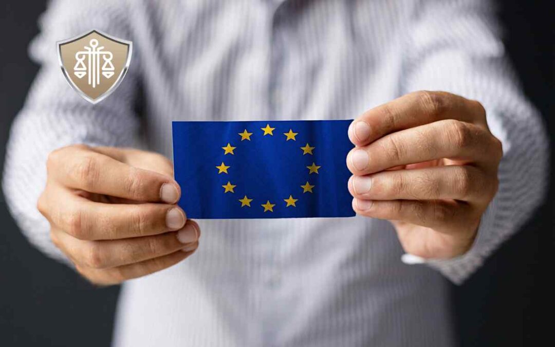 Dwie dłonie w jasnej koszuli trzymają małą, prostokątną kartkę z flagą Unii Europejskiej