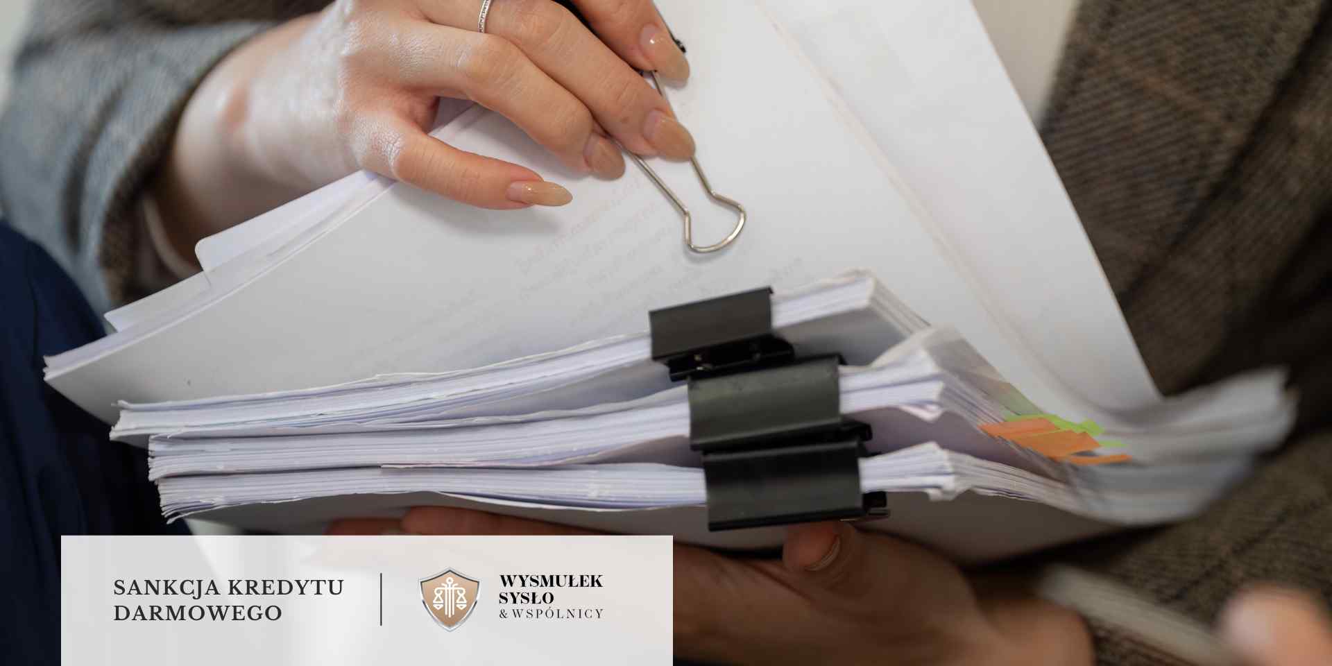 kredyt-konsumencki-sankcja-kredytu-darmowego Osoba trzyma w rękach plik dokumentów spiętych czarnymi klipsami
