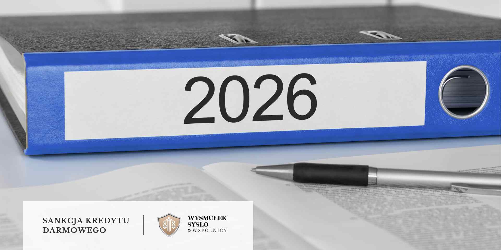 sankcja-kredytu-darmowego-2026-zasady Na pierwszym planie widać niebieski segregator z etykietą "2026", leżący na otwartym dokumencie obok długopisu