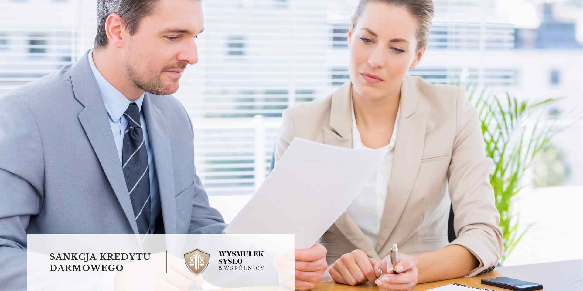 Mężczyzna w garniturze i kobieta w stroju biznesowym siedzą przy biurku i wspólnie analizują dokument trzymany przez mężczyznę.