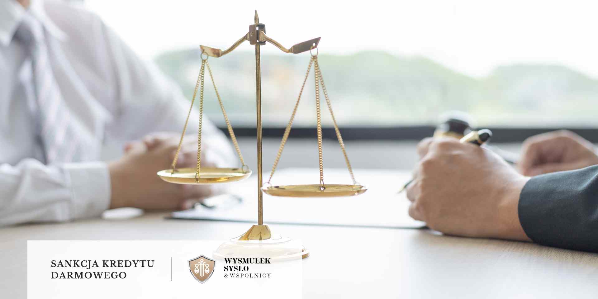 Zbliżenie przedstawia wagę szalkową symbolizującą sprawiedliwość, stojącą na biurku, przy którym dwie osoby, z których jedna trzyma długopis, prowadzą rozmowę