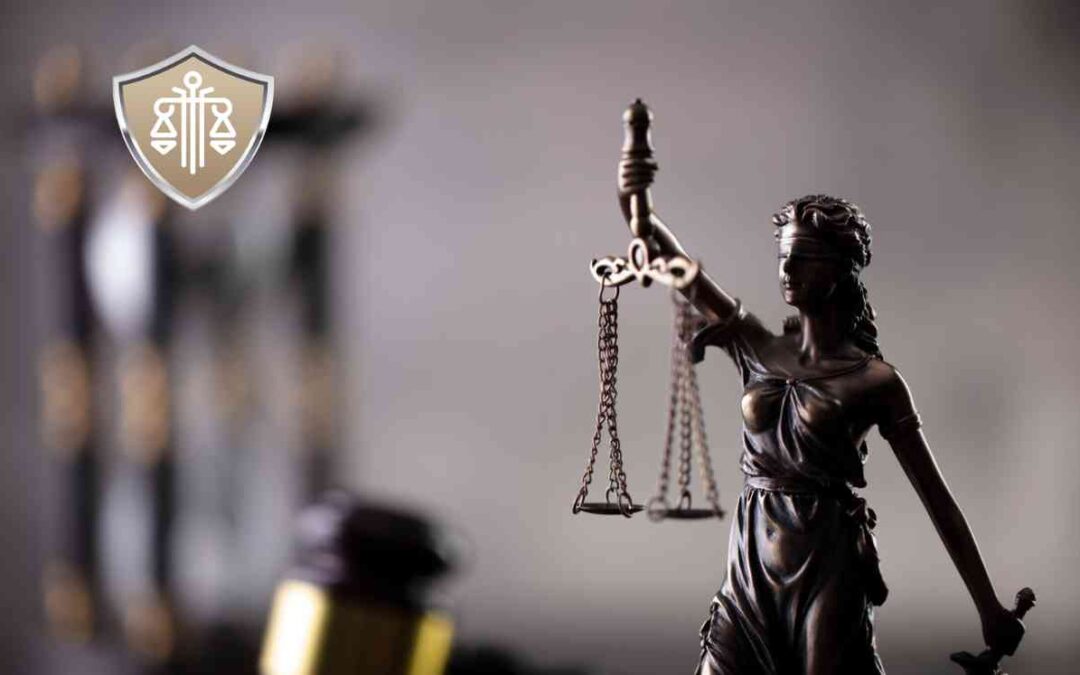 Bronze statue of Lady Justice holding scales, with a blurred gavel backdrop and a shield logo in the upper left corner.