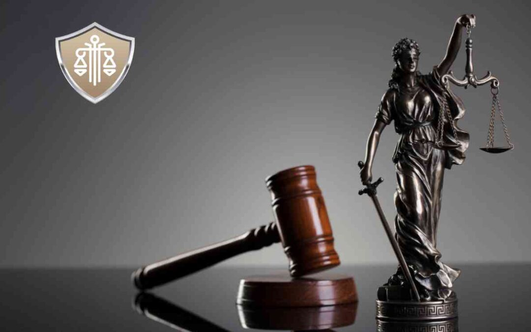 Posąg Temidy trzymającej wagę i miecz obok leżącego młotka sędziowskiego na ciemnym tle