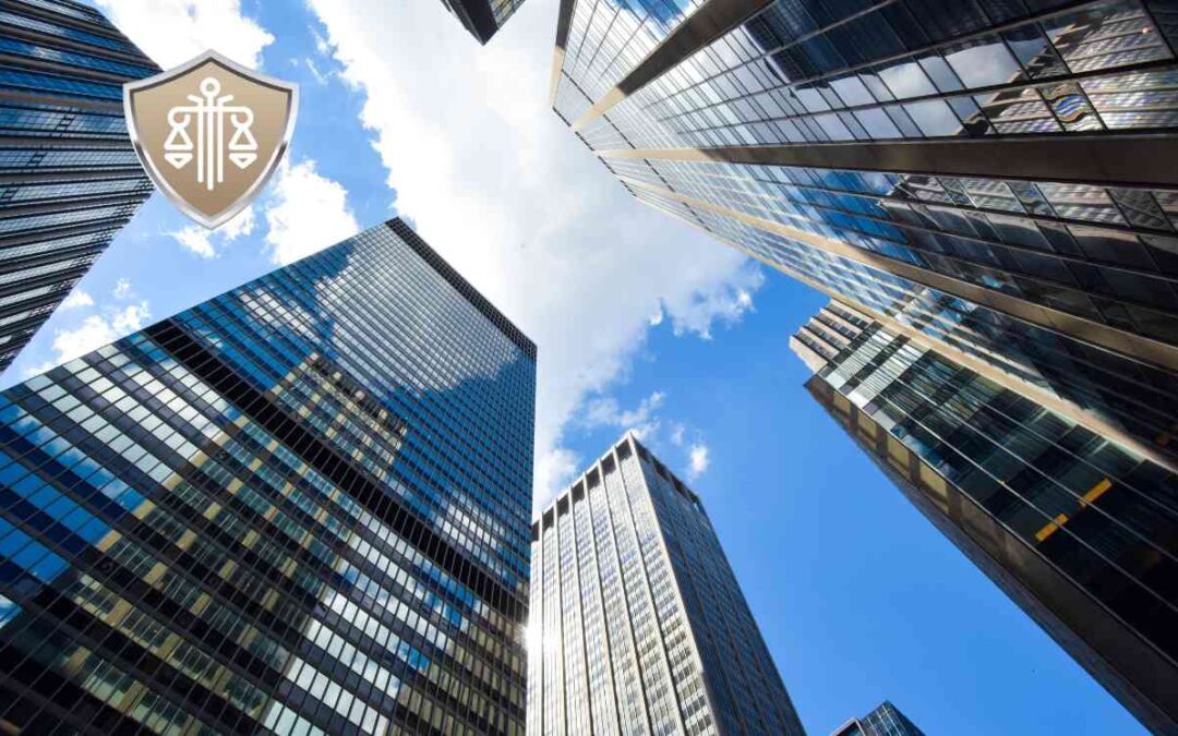 Low-angle view of skyscrapers with glass façades reaching toward a blue sky; a shield logo sits in the top-left corner.