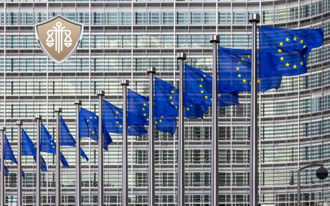 Row of European Union flags fluttering in front of a modern glass building, with a shield emblem in the upper left corner.