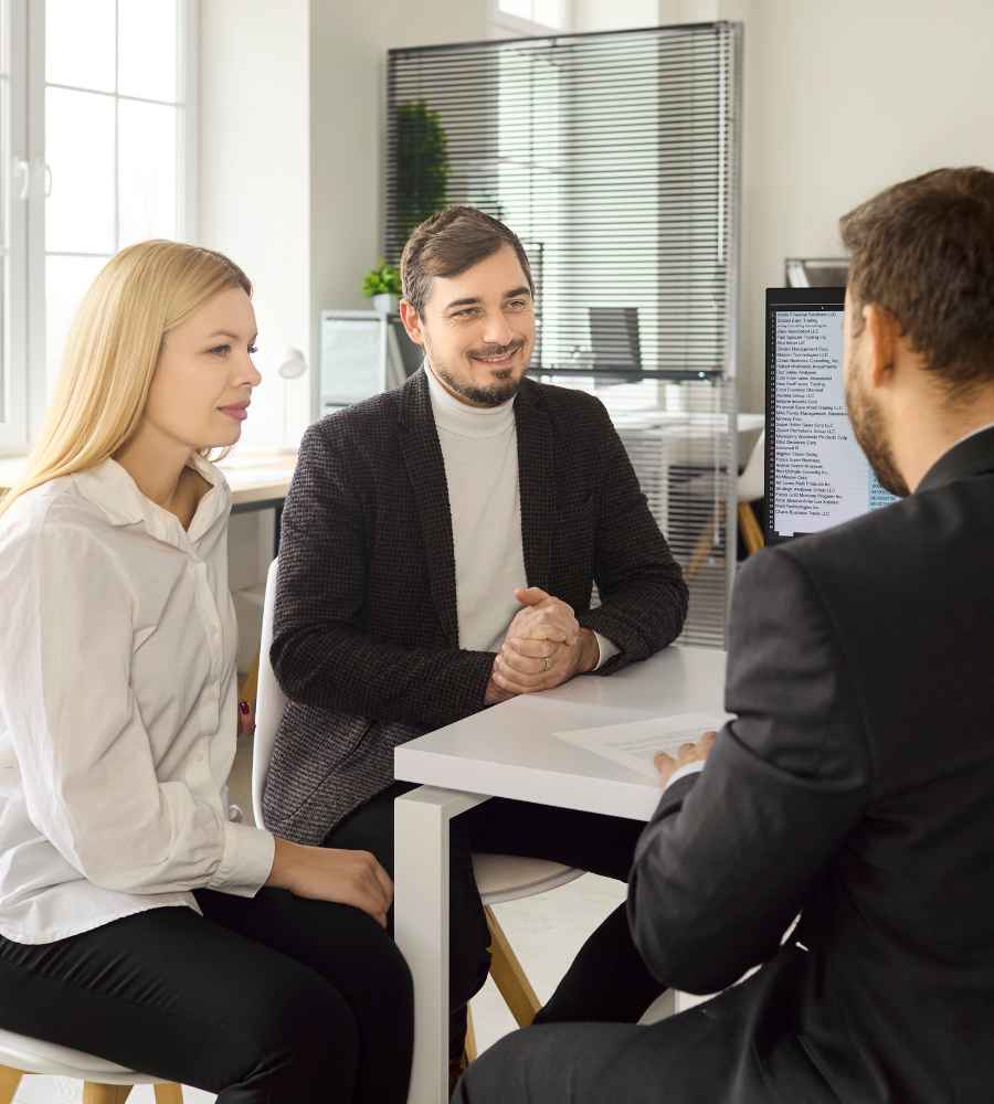 splacony-kredyt-konsumencki-a-analiza » Kancelaria Wysmułek, Sysło i Wspólnicy Professional meeting in a bright office: a man and a woman talk with a consultant across a white desk, with a monitor showing text nearby.
